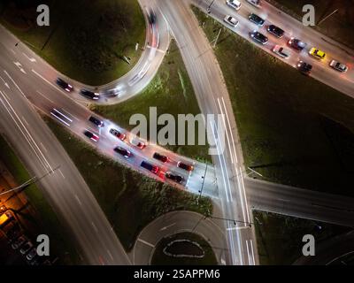 Von oben nach unten auf eine nächtliche Kreuzung mit einem sich bewegenden Verkehr. Fahrzeuge schaffen dynamische Lichtwege, die Geschwindigkeit, Bewegung und Moderne in der Stadt zum Ausdruck bringen Stockfoto
