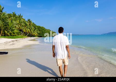 Isolierter Mann, der am unberührten weißen Sandstrand mit sanften Meereswellen am Morgen aus einem flachen Winkel spaziert, wird am Radhanagar Beach auf der Havelock Island aufgenommen Stockfoto