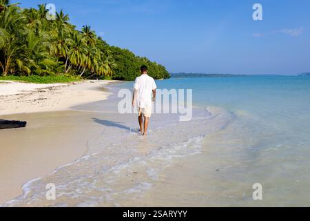Isolierter Mann, der am unberührten weißen Sandstrand mit sanften Meereswellen am Morgen aus einem flachen Winkel spaziert, wird am Radhanagar Beach auf der Havelock Island aufgenommen Stockfoto