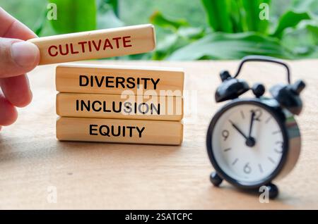 Pflegen Sie Text für Vielfalt, Inklusion und Gerechtigkeit auf Holzblöcken mit verschwommener Tischuhr. D- und I-Konzept. Stockfoto