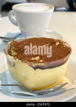 Tiramisu mit Kakao auf Untertasse mit Teelöffel bestreut. Essen und Getränke. Traditionelles italienisches Dessert. Cappuccino. Stockfoto