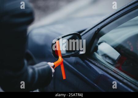 Eine Hand, die einen Schaber am Seitenspiegel eines Autos benutzt Stockfoto