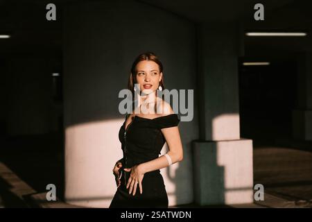 Frau in einem schwarzen Kleid posiert selbstbewusst in sanfter Beleuchtung mit Schatten und modernem Stil Stockfoto