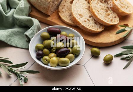 Frisch gebackener Brotlaib mit grünen und schwarzen Oliven in einer Schüssel, serviert auf einem hölzernen Schneidebrett, perfekt für einen mediterranen Snack oder Stockfoto
