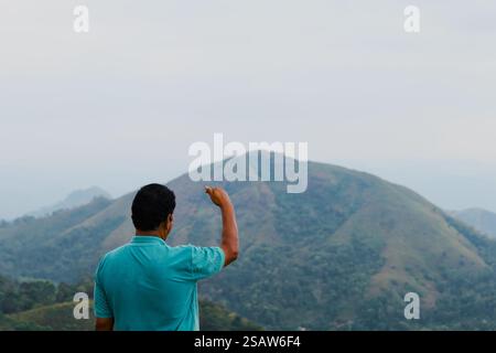 Ein Rückblick auf einen Mann, der auf dem Gipfel eines Berges steht und seine Hand triumphiert. Stockfoto