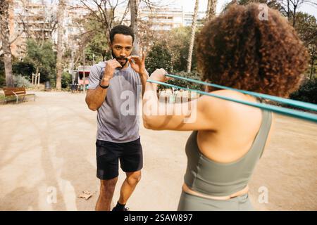 Ein persönlicher Trainer unterstützt einen Fitnesstrainer bei Übungen mit Widerstandsband im Freien im Park. Stockfoto