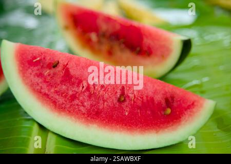 Nahaufnahme von saftigen roten Wassermelonenscheiben, die auf einem leuchtend grünen Bananenblatt angeordnet sind. Ein erfrischendes Sommererlebnis mit lebendigen Farben und Texturen. Stockfoto