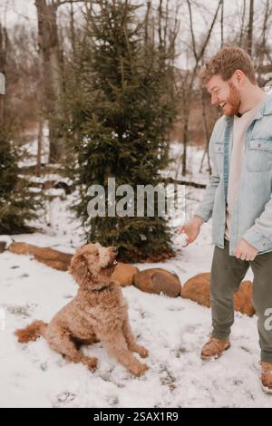 Ein glücklicher Kerl und Hund, der einen verschneiten Tag im Wald genießt Stockfoto