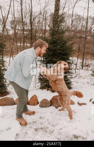 Ein glücklicher Kerl und Hund, der einen verschneiten Tag im Wald genießt Stockfoto