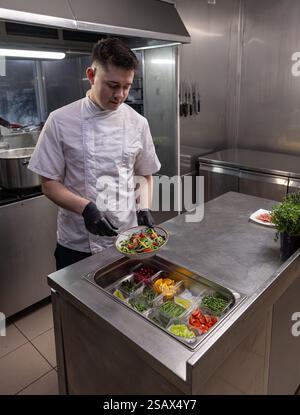 Koch, der bunten Salat in einer Restaurantküche zubereitet, eine gesunde und köstliche Mahlzeit zubereitet Stockfoto