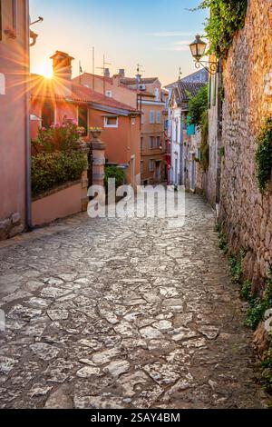 Rovinj, Kroatien - Blick auf eine leere, enge Kopfsteinpflasterstraße der Altstadt von Rovinj mit aufgehender Sonne, Sonnenstrahlen, traditionellen bunten Häusern und Stockfoto