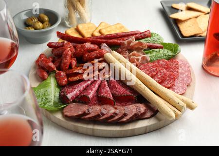 Verschiedene geräucherte Würstchen und andere Snacks serviert mit Wein auf weißem Tisch, Nahaufnahme Stockfoto