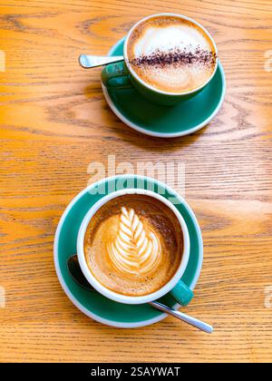 Zwei Kaffeetassen und Teelöffel auf einem bewaldeten Tisch in einem Café Stockfoto