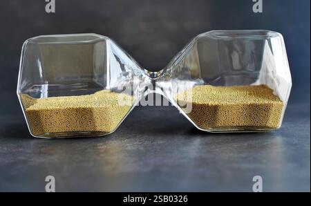 Nahaufnahme Verlegung seitlich transparentes Sanduhr mit goldenem Sand, Sandglas im dunklen Hintergrund, Zeitstopp- oder Balance-Zeitkonzept, für Werbung Stockfoto