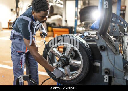 Professioneller Mechaniker, der einen Autoreifen auf fortschrittlichen Maschinen in einer modernen Autowerkstatt ausbalanciert und sein Können und seine Präzision im Kfz-Service unter Beweis stellt Stockfoto