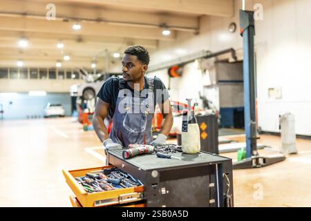 Junger Mechaniker, der in einer professionellen Garage an einem Auto arbeitet, mit Werkzeugen und Ausrüstung für Wartungs- und Reparaturarbeiten Stockfoto