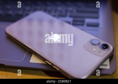 Smartphone mit sichtbarem Logo, das auf einem Laptop liegt und eine reflektierende Oberfläche erzeugt Stockfoto