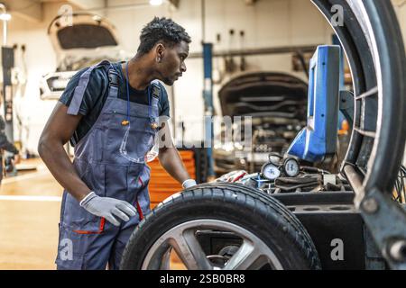 Professioneller Mechaniker, der ein digitales Reifendruckmessgerät während einer Radwartung in einer stark frequentierten Autowerkstatt verwendet Stockfoto