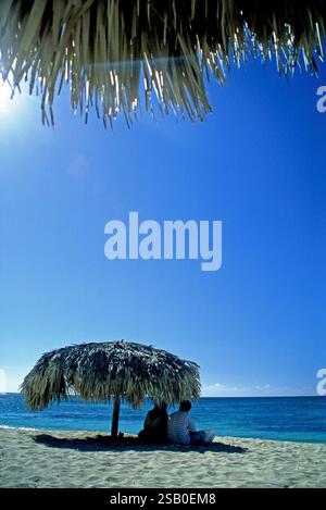 Kuba, Sancti Spiritus, Playa Ancon 01. Juni 2020 - in der Nähe von Trinidad. Leute, die unter einem Sonnenschirm aus Palmblättern sitzen. Stockfoto