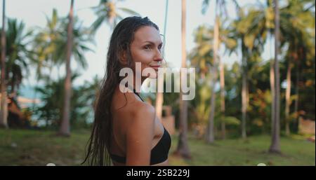 Eine Frau im Bikini steht selbstbewusst vor der Kulisse üppiger Palmen in Thailand. Die Szene wird in festgehalten und unterstreicht die Schönheit der tropischen Umgebung. Stockfoto