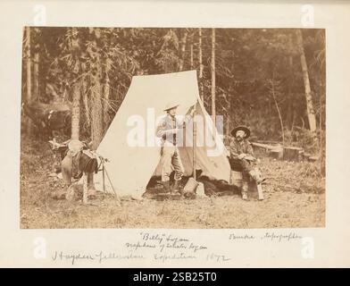 Zufallsdaten, Datensätze, von, A, Lebensdauer, 1846-1931, [tatsächlich 1932]., zwei Männer stehen auf einer Waldlichtung und posieren neben einem provisorischen Zelt. Ein Mann trägt einen Anzug mit einem Bowler-Hut und hält einen großen Wanderstock, während der andere, in Outdoor-Kleidung gekleidet, sich lässig an das Zelt lehnt. Im Vordergrund sitzen zwei kleine Hunde aufmerksam auf dem Boden, scheinbar von ihrer Umgebung fasziniert. Die natürliche Landschaft mit hohen Bäumen bildet eine ruhige Kulisse und lässt auf ein gemütliches Outdoor-Abenteuer oder einen Campingausflug schließen. In der unteren rechten Ecke ist eine handschriftliche Notiz, die die Position angibt Stockfoto