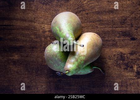 Drei grüne Birnen sitzen auf einem Holztisch. Die Birnen sind reif und verzehrfertig Stockfoto