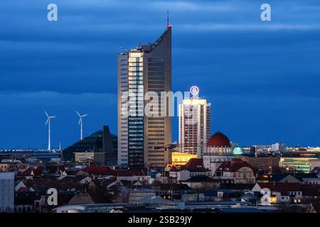 Sonnenuntergang in Leipzig. Universitätsturm und Wintergarten Hochhaus vor dunklem Himmel. Windräder drehen sich im Hintergrund. Aufnahme mit Teleobjektiv. Stockfoto
