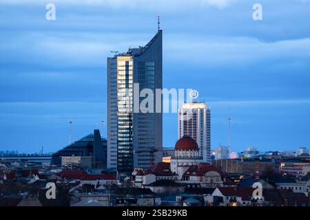Universitätsturm und Wintergarten Hochhaus am Abend. Atmosphäre bei Sonnenuntergang in Leipzig. Gebäude sind beleuchtet. Windturbinen sind zu sehen. Stockfoto