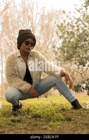 Eine stilvolle schwarze Frau mit Sonnenbrille, Mütze und modischem Outfit posiert selbstbewusst im Freien. Stockfoto