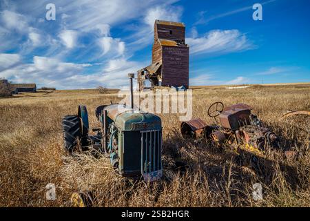 Ein alter Traktor sitzt auf einem Feld neben einem Getreidesilo. Der Traktor ist verrostet und hat ein gebrochenes Vorderrad Stockfoto
