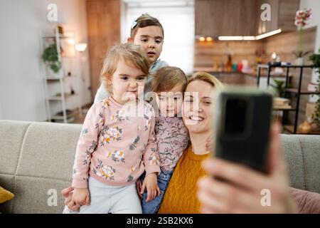 Mutter und ihre drei Töchter sitzen auf der Couch und machen ein Selfie im Wohnzimmer zu Hause. Stockfoto