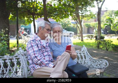 Ein älteres Paar sitzt auf einer Parkbank und schaut auf ein Handy. Stockfoto