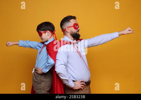 Vater und Sohn tragen Superheldenkostüme auf orangem Hintergrund Stockfoto