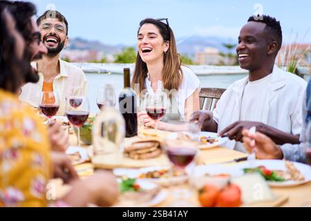 Gruppe von verschiedenen jungen Erwachsenen fröhliche Freunde Barbecue Sommerparty Wiedersehen essen auf dem Dach Stockfoto