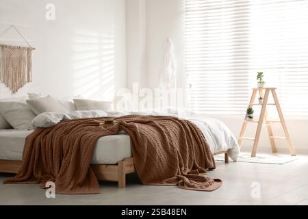 Großes Bett mit Decke im Mokkakeschatten drinnen. Stilvolle Inneneinrichtung des Schlafzimmers in trendigen Farben von 2025 Jahren Stockfoto