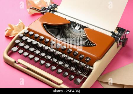 Vintage Schreibmaschine, zerknittertes Papier und Umschlag auf rosa Hintergrund, Nahaufnahme Stockfoto