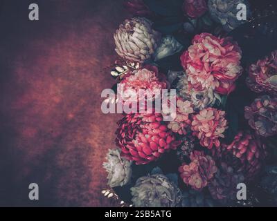 Ein üppiger Blumenstrauß aus rosa und weißen Blumen liegt vor einem dunklen, strukturierten Hintergrund. Goldene Akzente sorgen für einen Hauch von Eleganz. Stockfoto