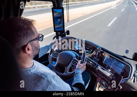 Lkw-Fahrer, der einen Lkw auf einer Autobahn fährt, mit Armaturenbrett, Lenkrad und Rückspiegel im Vordergrund. Stockfoto