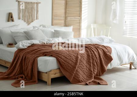 Großes Bett mit Decke im Mokkakeschatten drinnen. Stilvolle Inneneinrichtung des Schlafzimmers in trendigen Farben von 2025 Jahren Stockfoto