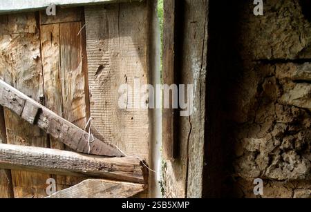 Eine Nahaufnahme einer verwitterten Holztür mit einem gerissenen und alten Holzrahmen, der den Verlauf der Zeit zeigt. Stockfoto
