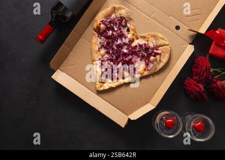 Valentinstag herzförmige süße Pizza mit Ananas in Pappkarton auf schwarzem Hintergrund. Romantisches Abendessen mit Rotwein und Geschenk. Fastfood Stockfoto