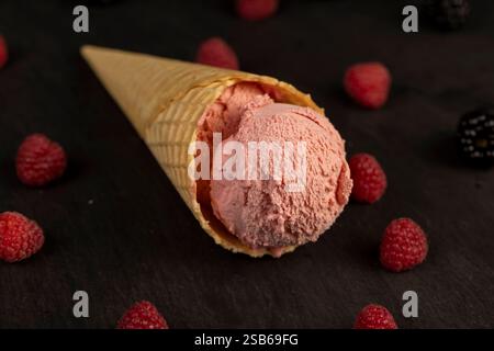 Rosafarbenes Eis mit Himbeergeschmack und roten Himbeerbeeren auf einem schwarzen Schieferbrett, Nahaufnahme von Eis mit Beerengeschmack und frischer Himbeere Stockfoto