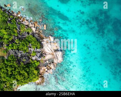 Aus der Vogelperspektive der La Digue Küste auf den Seychellen mit lebendigem türkisfarbenem Wasser, großen Felsformationen entlang des Ufers und dichter grüner Vegetation Stockfoto