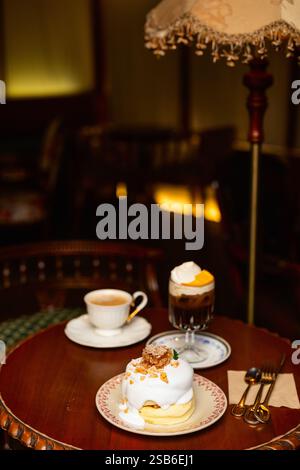 Ein warmes, gemütliches Café mit einem Teller flauschiger Pfannkuchen mit Sahne und Wabencreme, einer Tasse Kaffee und einem Eiskaffee mit Schlagsahne Stockfoto
