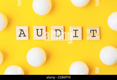 Gelber Hintergrund mit weißen Kugeln. Das Wort Audit wird in schwarzen Buchstaben im Hintergrund geschrieben, wobei jeder Buchstabe einen Holzblock darstellt. Stockfoto