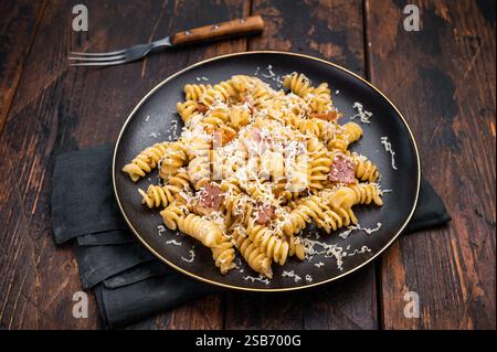 Italienische Carbonara-Pasta mit knusprigen Speckstückchen auf einem Teller. Hölzerner Hintergrund. Draufsicht. Stockfoto