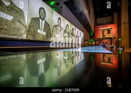 Greensboro Lunch Counter Sit-ins-Ausstellung im National Museum of African American History and Culture in Washington DC | WASHINGTON D.C., Vereinigte Staaten — Fahndungsfotos von Demonstranten der Bürgerrechte leuchten über einem reflektierenden schwarzen Zähler im National Museum of African American History and Culture, Teil einer Galerie über den Widerstand der Jim Crow-Ära. In der Nähe befindet sich ein Wachturm aus dem Louisiana State Penitentiary in Angola, eines der großen Artefakte des Museums, das während der Bauarbeiten im Jahr 2013 in das Gebäude eingebracht wurde. Ein Kind untersucht die Anzeige vom Rand des Wassers aus. Stockfoto