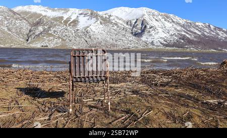 Ruhige Winterlandschaft mit trockenem Gras, wankendem Schilf, schneebedeckten Bergen und einem ruhigen See unter einem klaren blauen Himmel in einer friedlichen Landschaft. Stockfoto