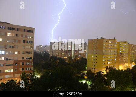 Ein dramatischer Blick auf eine Budapester Wohnsiedlung durch ein Fenster, mit dunklen schwarzen Wolken und einem Blitzschlag, der den stürmischen Himmel über der Stadt beleuchtet Stockfoto