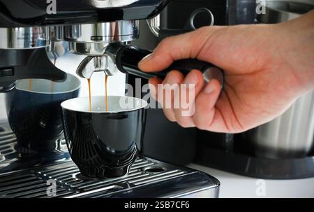Nahaufnahme einer männlichen Hand, die einen Portafilter hält und zu Hause mit einer modernen Kaffeemaschine frischen aromatischen Kaffee zubereitet. Machen Sie eine Tasse Kaffee Stockfoto